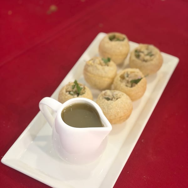 Pani Puri, a popular Indian street food, served on a white rectangular plate with a small pitcher of pani.