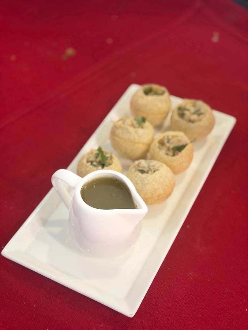 Pani Puri, a popular Indian street food, served on a white rectangular plate with a small pitcher of pani.