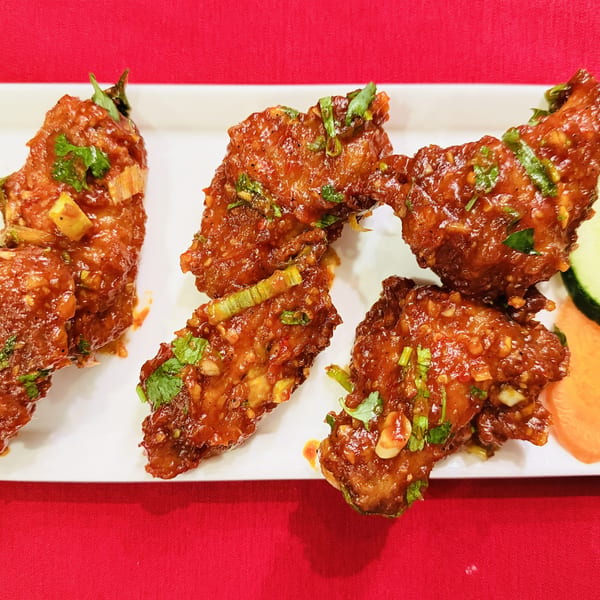 Four spicy chicken wings garnished with cilantro and green onions, served with cucumber and carrot slices.