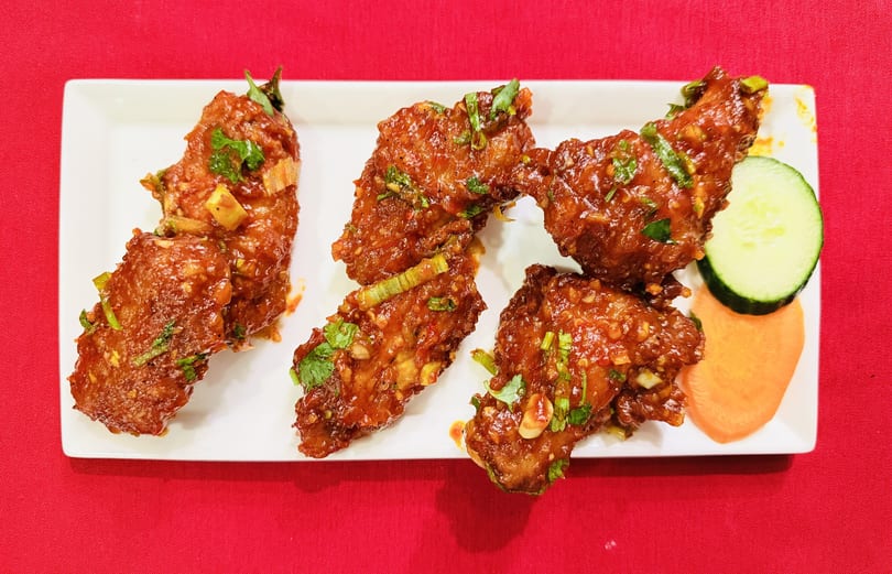 Four spicy chicken wings garnished with cilantro and green onions, served with cucumber and carrot slices.