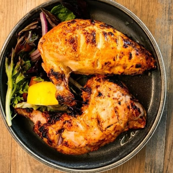 Grilled chicken breast and leg with a side salad and lemon wedge on a dark plate.