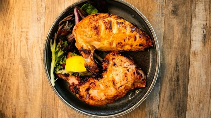 Grilled chicken breast and leg with a side salad and lemon wedge on a dark plate.