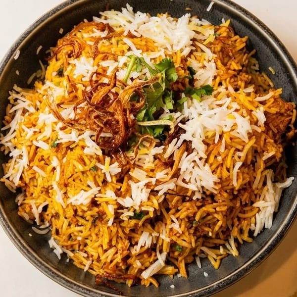 A large bowl of biryani with white and orange rice, topped with fried onions and cilantro.