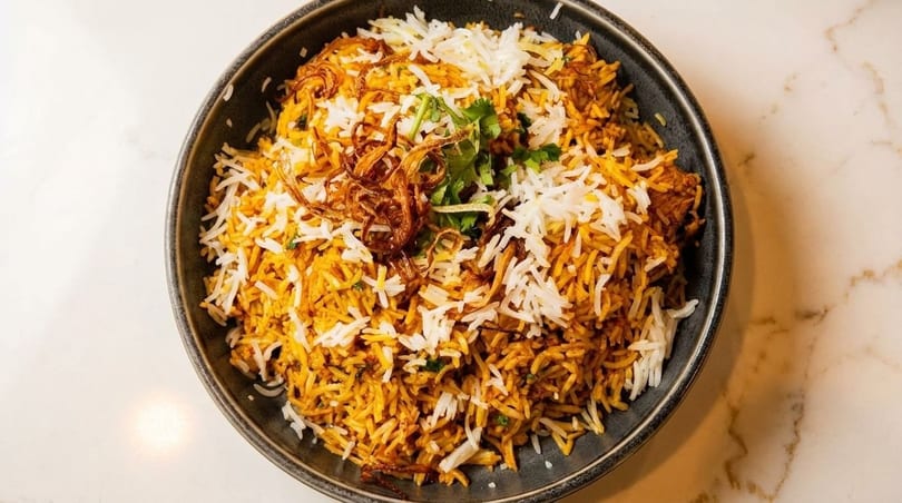 A large bowl of biryani with white and orange rice, topped with fried onions and cilantro.