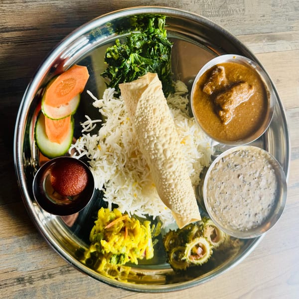Nepalese thali platter with basmati rice, papad, curry, dal, saag, cauliflower, pickles, and gulab jamun on a steel plate.